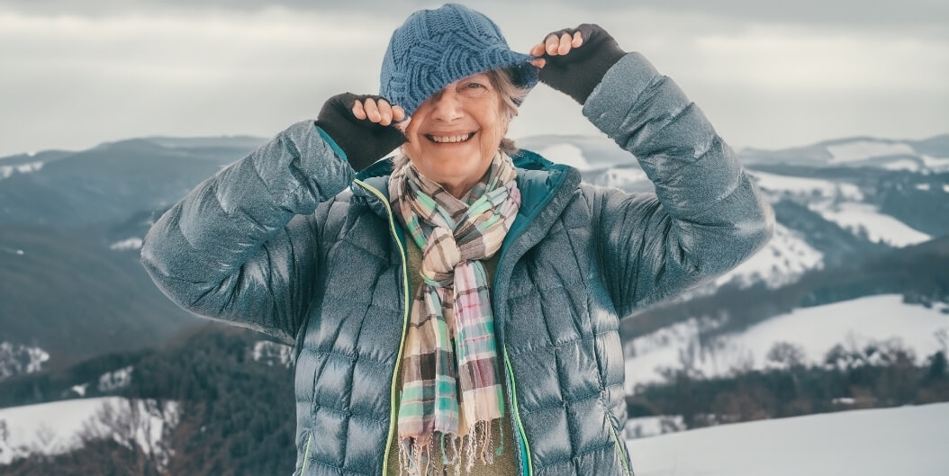 Elderly Woman in Winter Coat and Gloves Smiling Outdoors in the Snow at an Independent Living Facility