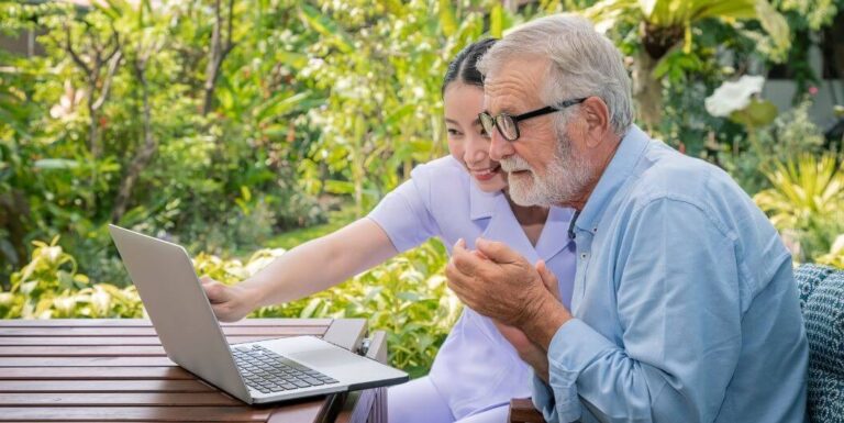 Female Nurse Helping Elderly Man with Laptop at Independent Living Facility