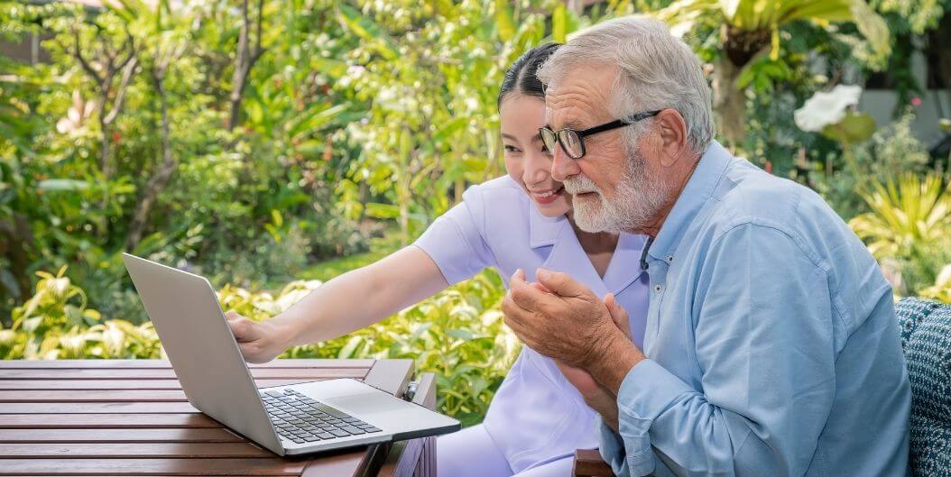 Female Nurse Helping Elderly Man with Laptop at Independent Living Facility