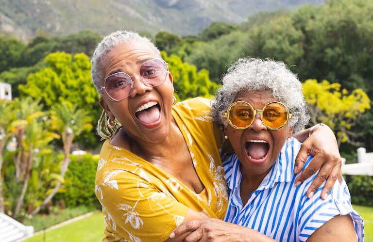 Two Excited Elderly Women in Sunglasses Embracing Outdoors at an Independent Living Community